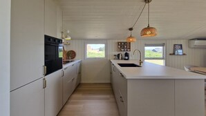Ett modernt kök med vita skåp, en köksö med diskho och hängande lampor.
