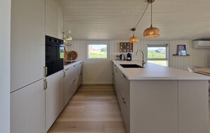 Eine moderne Küche mit weißen Schränken, einer zentralen Kochinsel mit Spüle und Pendelleuchten.