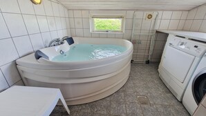 Ett badrum med ett inbyggt bubbelbadkar, ett fönster, en tvättmaskin och ett kaklat golv.