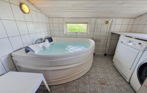 Ein Badezimmer mit Eckbadewanne, Fenster, Waschmaschine und Fliesenboden.