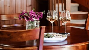 Une table de salle à manger en bois, avec deux verres à vin et une assiette de nourriture, entourée de chaises en bois.
