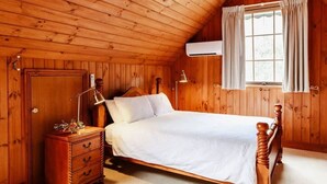 Une chambre aux murs lambrés, avec un lit simple, une table de chevet, une commode et une fenêtre avec des rideaux.