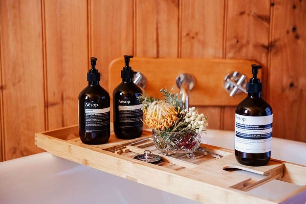A wooden tray with three bottles of Aesop products and a glass bowl with dried flowers.