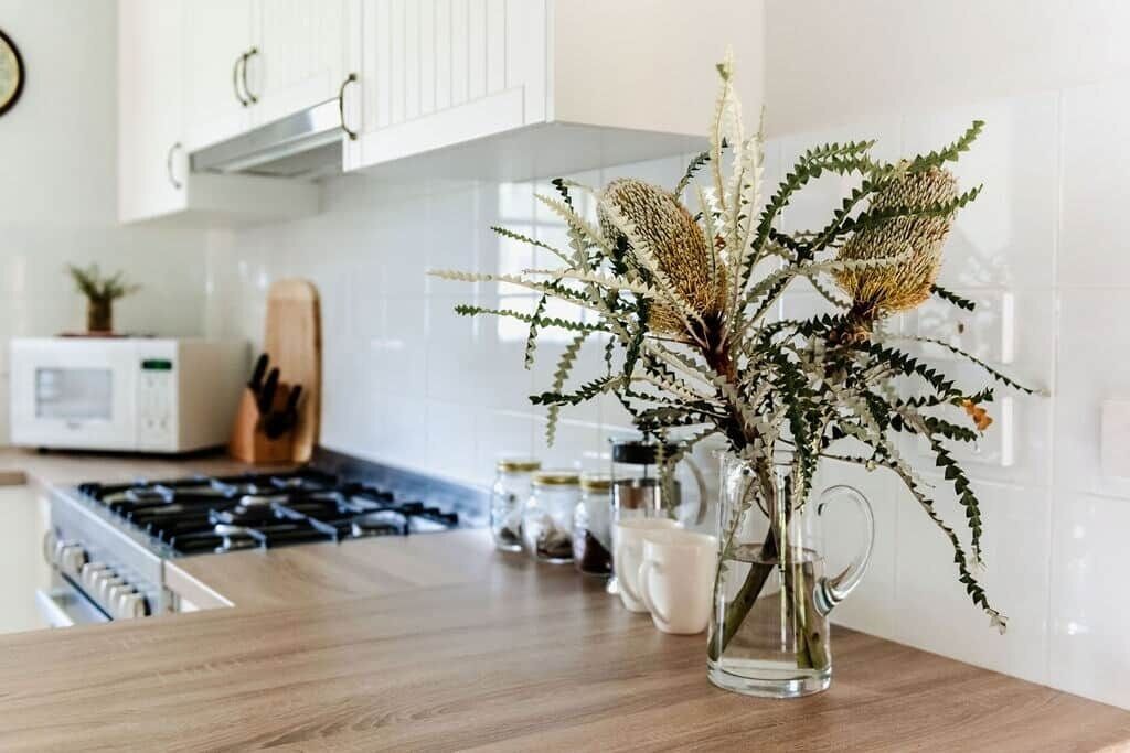 Een keuken met een houten aanrecht, een glazen vaas met gedroogde bloemen, en een magnetron op de achtergrond.