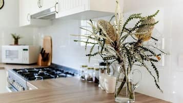 Een keuken met een houten aanrecht, een glazen vaas met gedroogde bloemen, en een magnetron op de achtergrond.