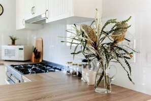A kitchen with a wooden countertop, a clear glass vase with dried flowers, and a microwave in the background. - The Cottage at Paramoor Winery (Carlsruhe)