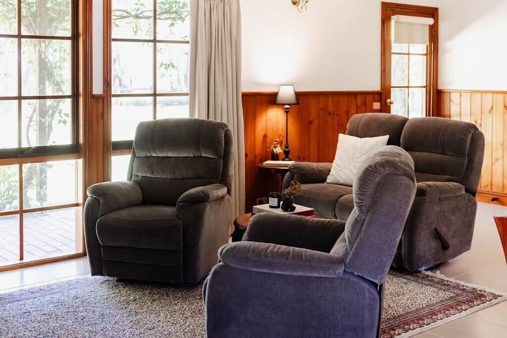 A room with two reclining chairs, a small table with a lamp, and a view through large windows.