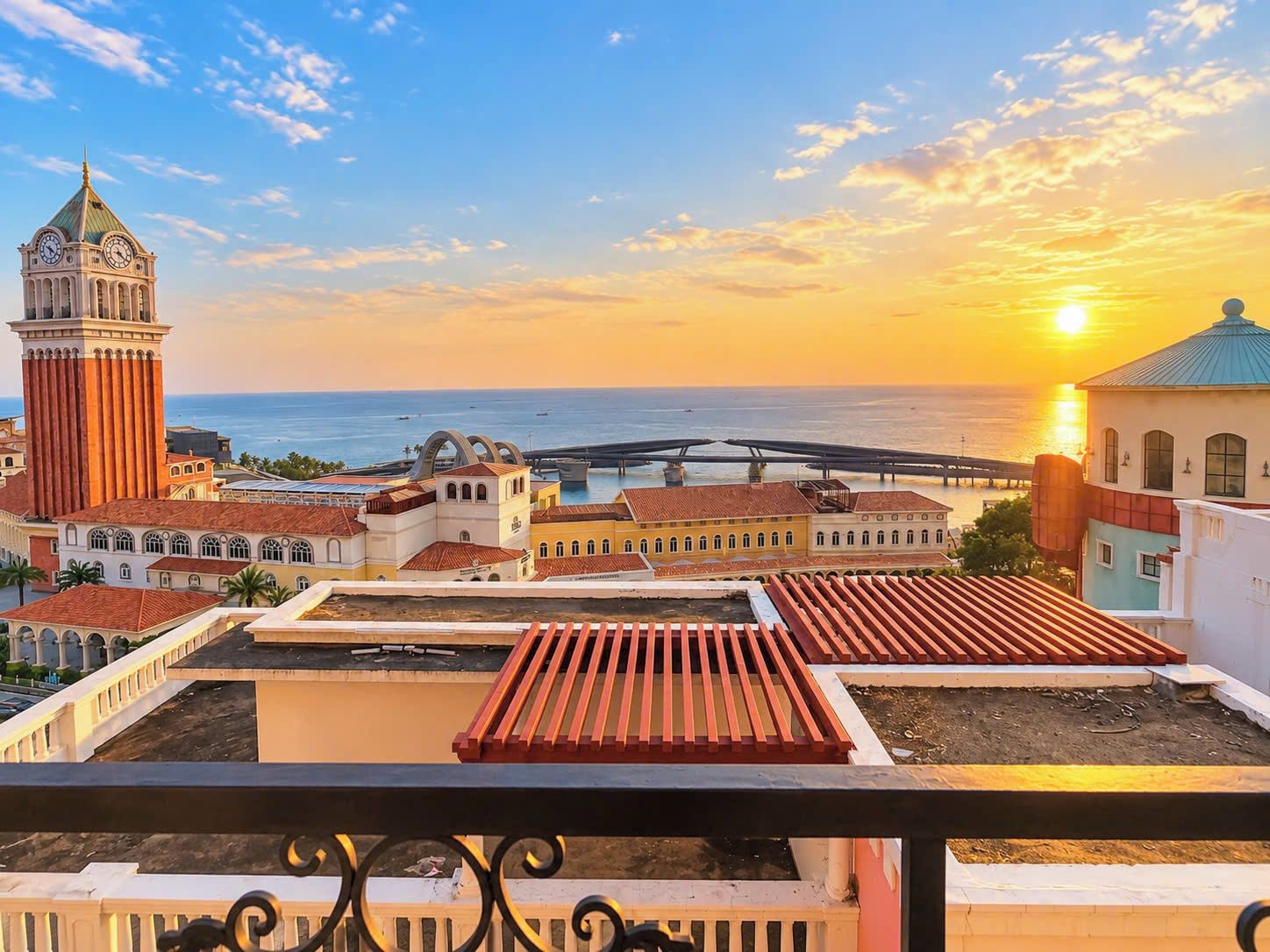 Un paisaje urbano costero con una imponente torre del reloj, un puente y una puesta de sol sobre el mar.