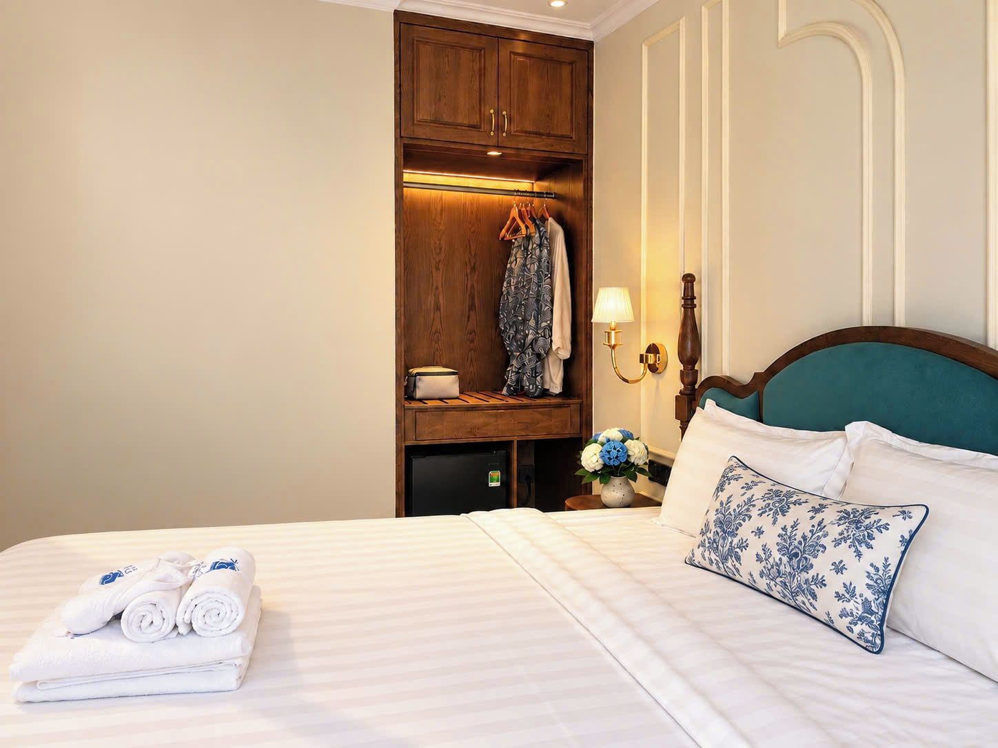 Una habitación de hotel con cama, armario de madera, mesita de noche y lámpara.