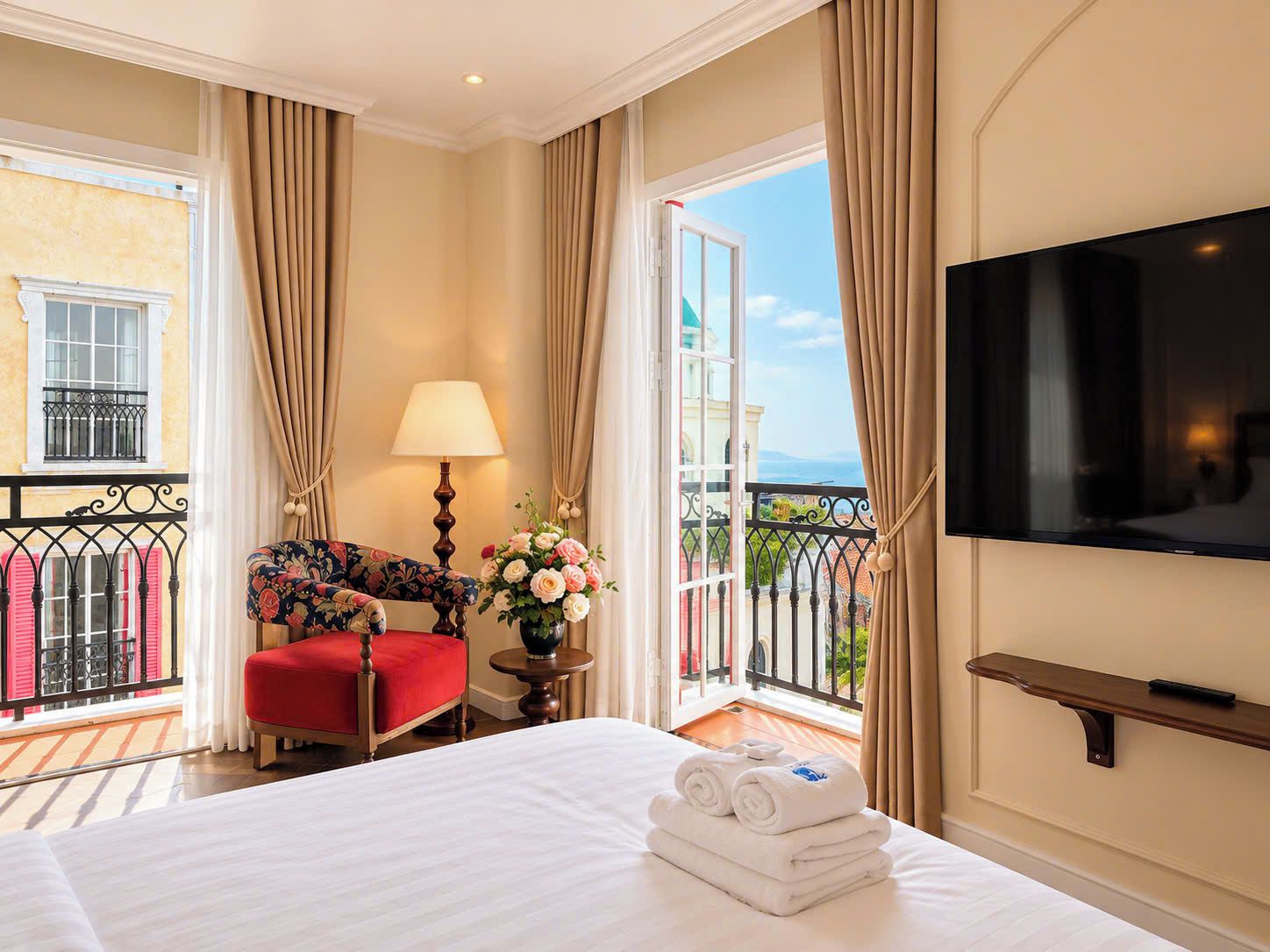 A hotel room with a bed, a TV, a balcony with a view, and a red chair.