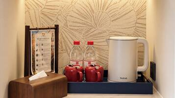 A hotel room with a framed welcome sign, a tissue box, two red mugs, a white coffee pot, and a Tefal kettle on a marble countertop.