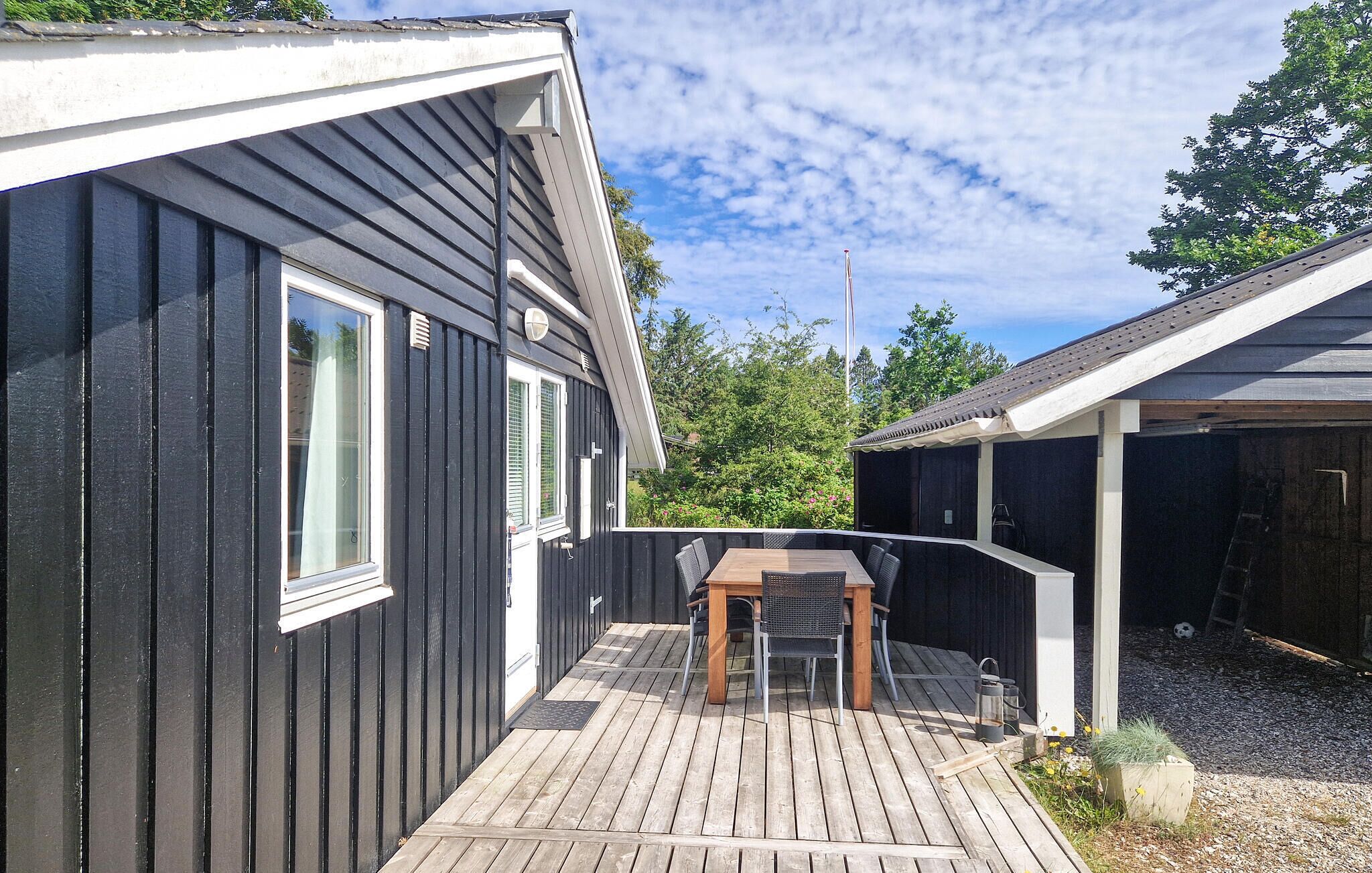 A deck with a table and chairs, a covered outdoor area, and a building with a dark exterior and white trim.