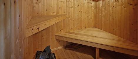 A wooden sauna room with benches and a stone container.