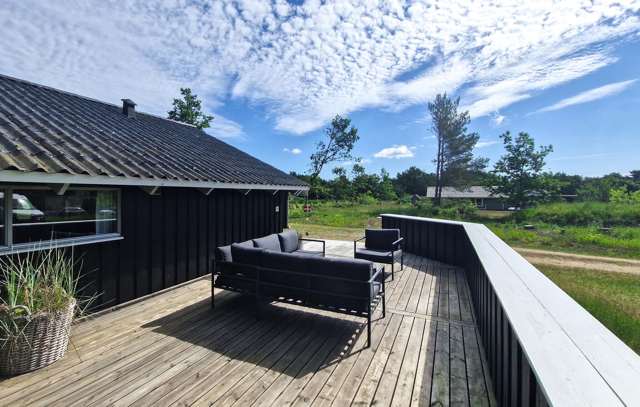 A wooden deck with outdoor furniture, a building with a metal roof, and a natural landscape in the background.