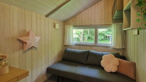 A cozy room with a wooden wall, a star decoration, a green sofa with a flower pillow, and a window with a view of greenery. - Nice home in ålbæk with sauna (Ålbæk)