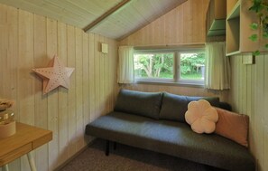 Ein gemütliches Zimmer mit Holzwand, einer Sterndeko, einem grünen Sofa mit einem blumigen Kissen und einem Fenster mit Blick ins Grüne.