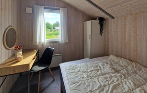 Ein Schlafzimmer mit Bett, Schreibtisch mit Stuhl, Kleiderschrank, Fenster mit Vorhängen und Heizkörper.