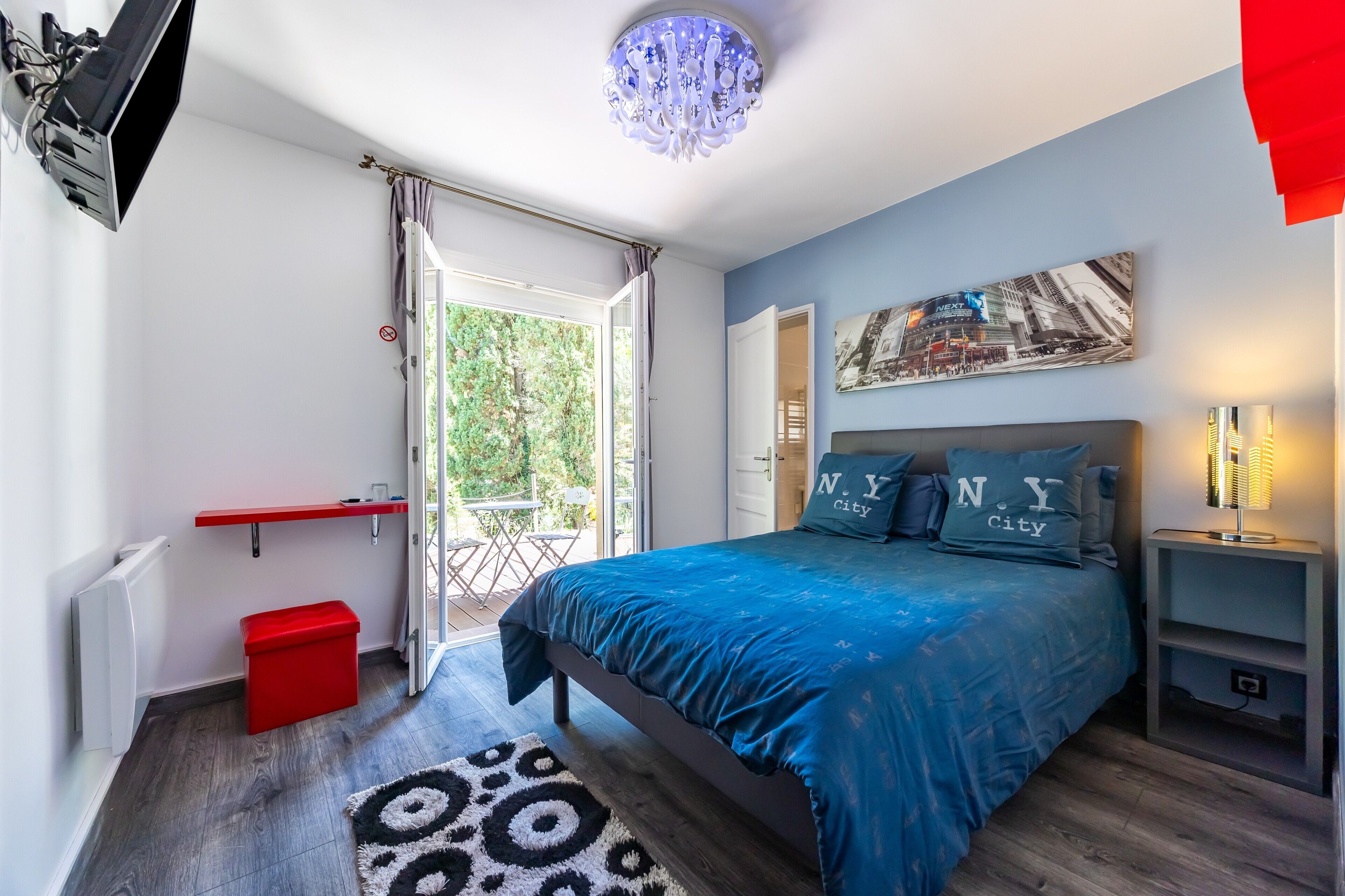A bedroom with a bed, a red trash bin, a ceiling light fixture, and a window with curtains.