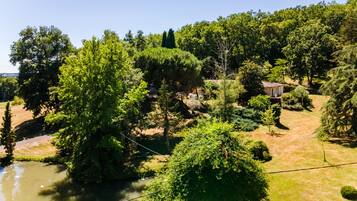 A riverside property with a small building, lush greenery, and a clear sky.