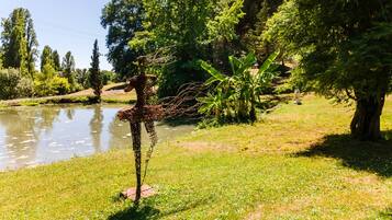 Une sculpture de girafe se trouve dans une zone herbeuse, avec un étang et des arbres en arrière-plan.