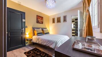 A bedroom with a bed, bedside lamps, a nightstand, a dresser, a mirror, a window with curtains, and a door.