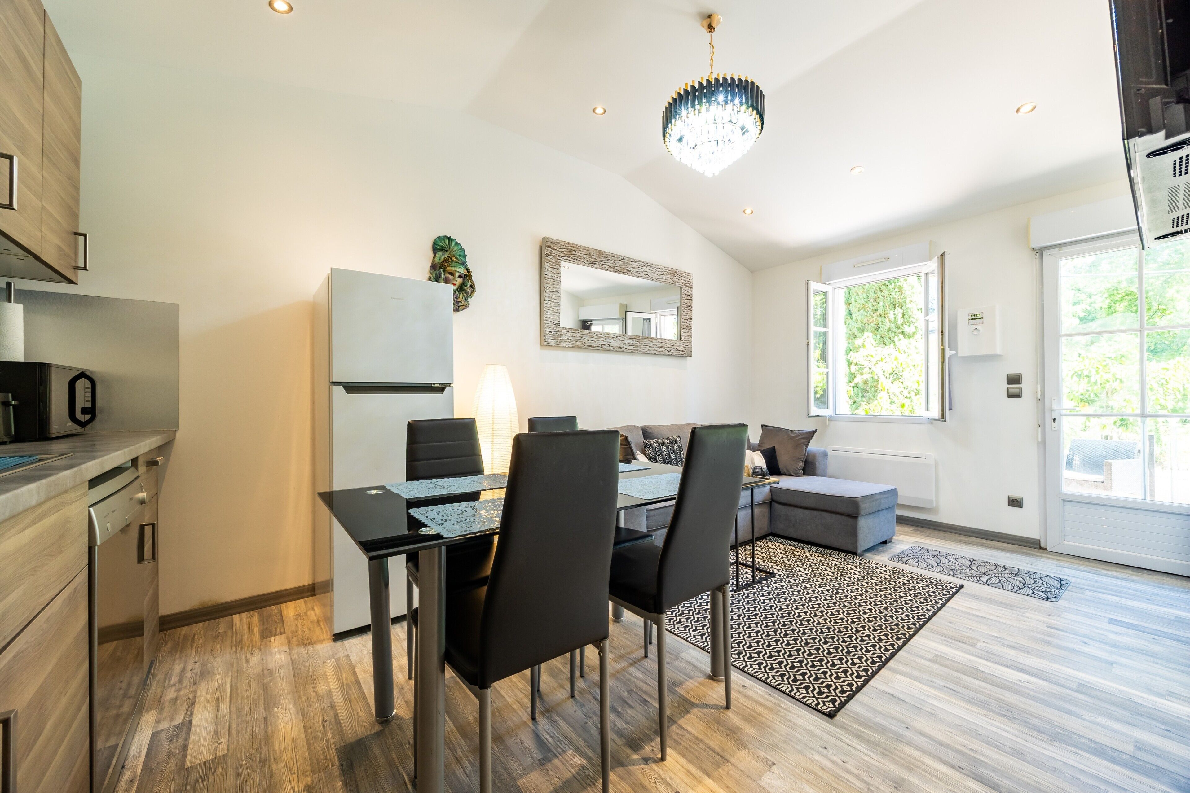 A modern kitchen with a dining area, a large mirror, and a view of greenery outside.