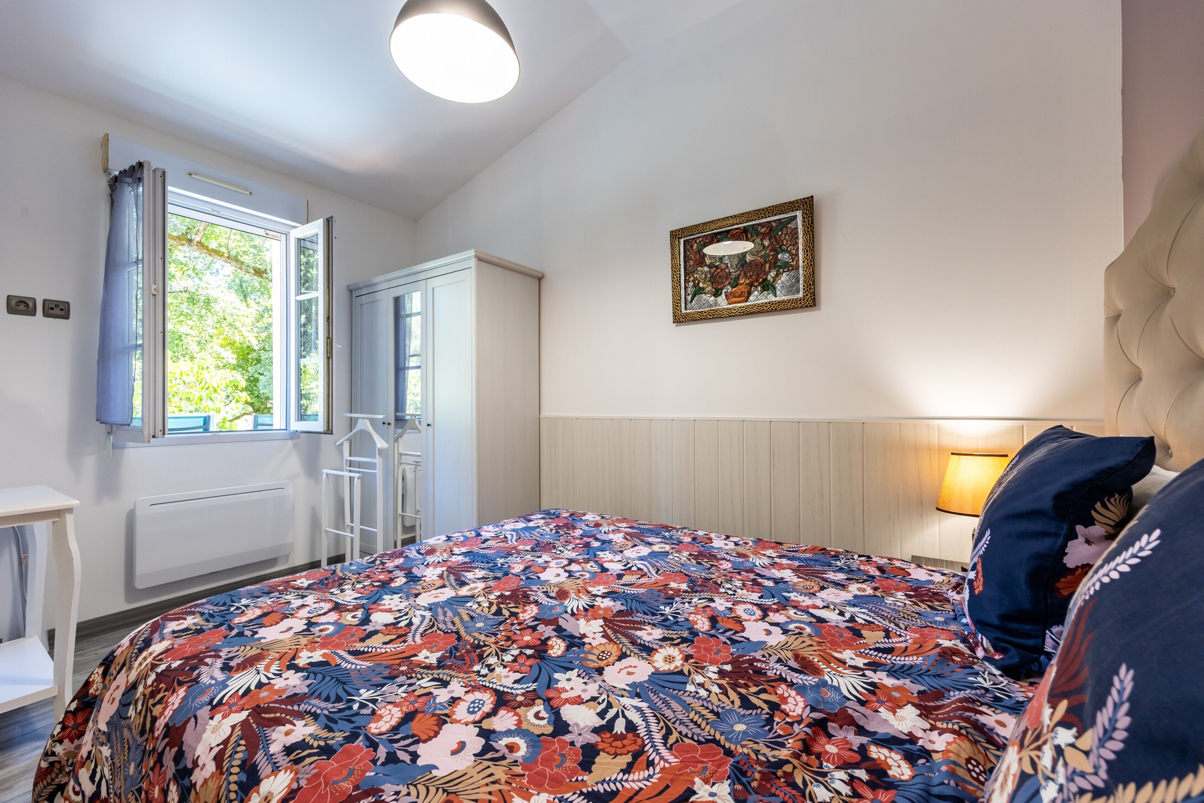 A bedroom with a bed, a window, a radiator, and a wall-mounted picture.