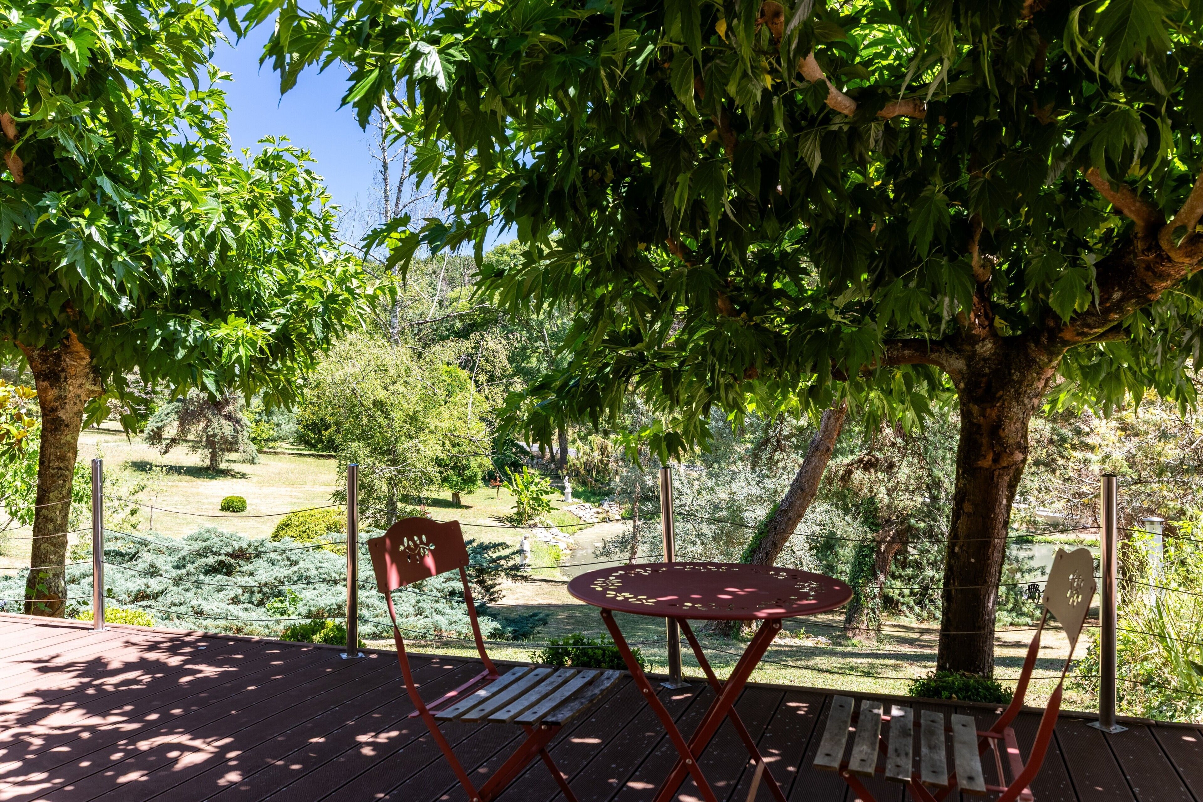 A wooden deck with a table and chairs, surrounded by trees and a garden.