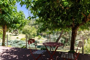 Una terraza de madera con una mesa y sillas, rodeada de árboles y un jardín.