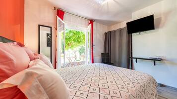A bedroom with a bed, a television, a window with curtains, and a door leading outside.