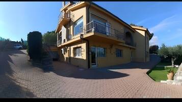 A two-story building with a balcony, a driveway, and a small garden area.
