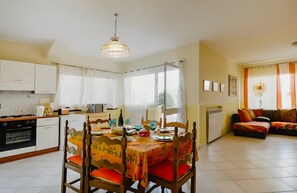 A dining area with a table set for four, a kitchen with modern appliances, and a living room with a sofa and curtains. - Apartment 'Viola' with Sea View, Shared Pool and Wi-Fi (Poggi)
