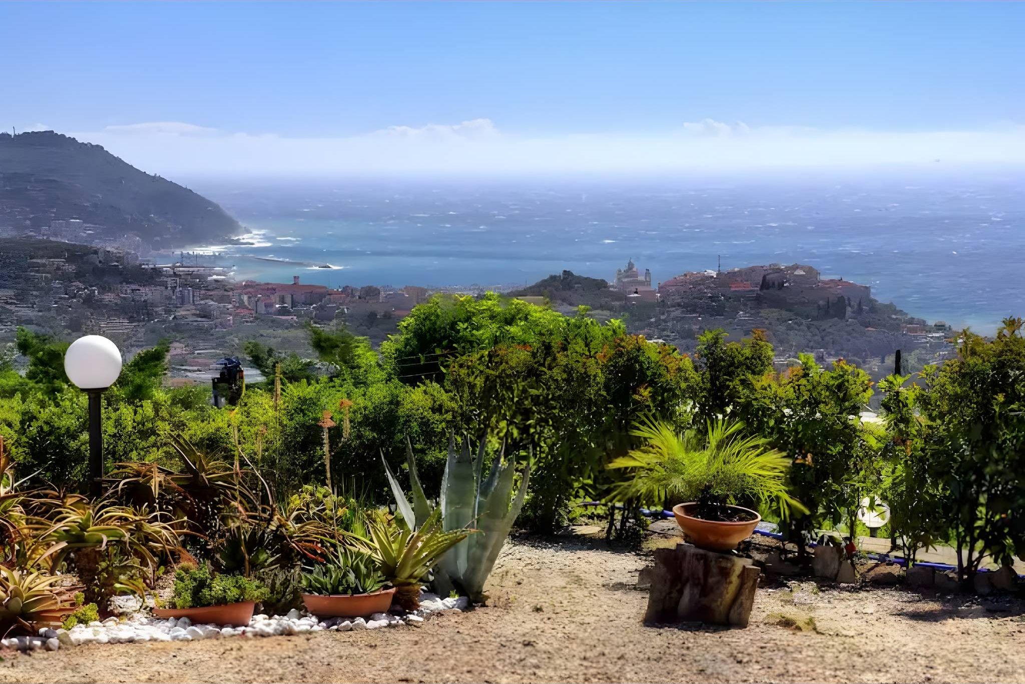 Ein Garten mit verschiedenen Pflanzen und Blick auf eine Küstenstadt.