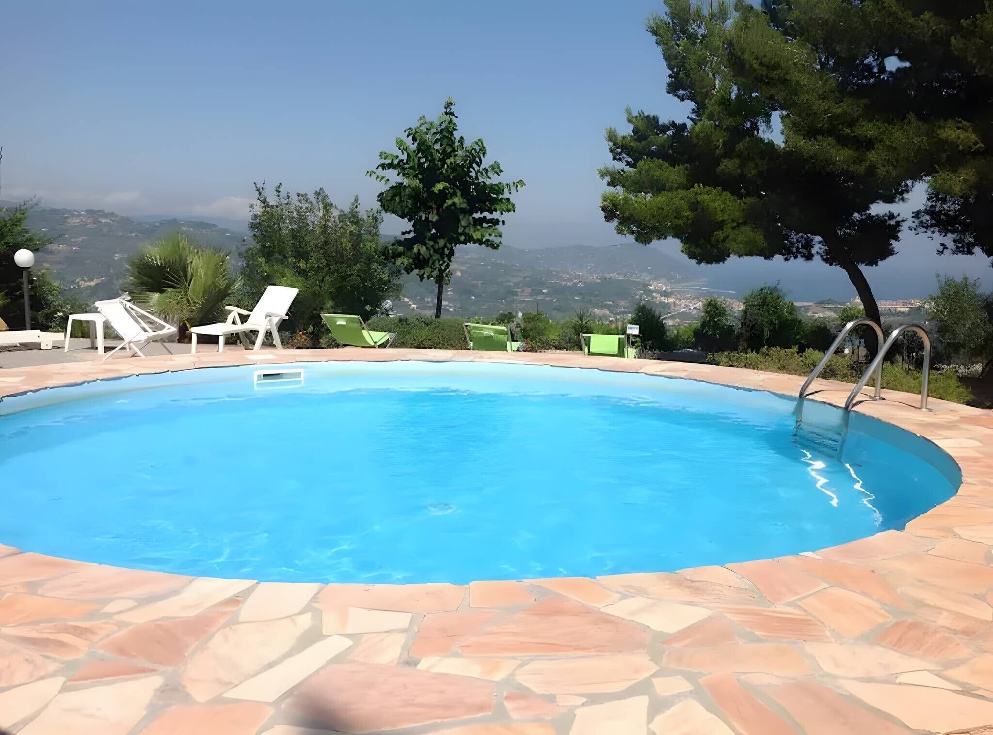 Piscina com ladrilhos de pedra, rodeada por espreguiçadeiras e vista para colinas ao longe.