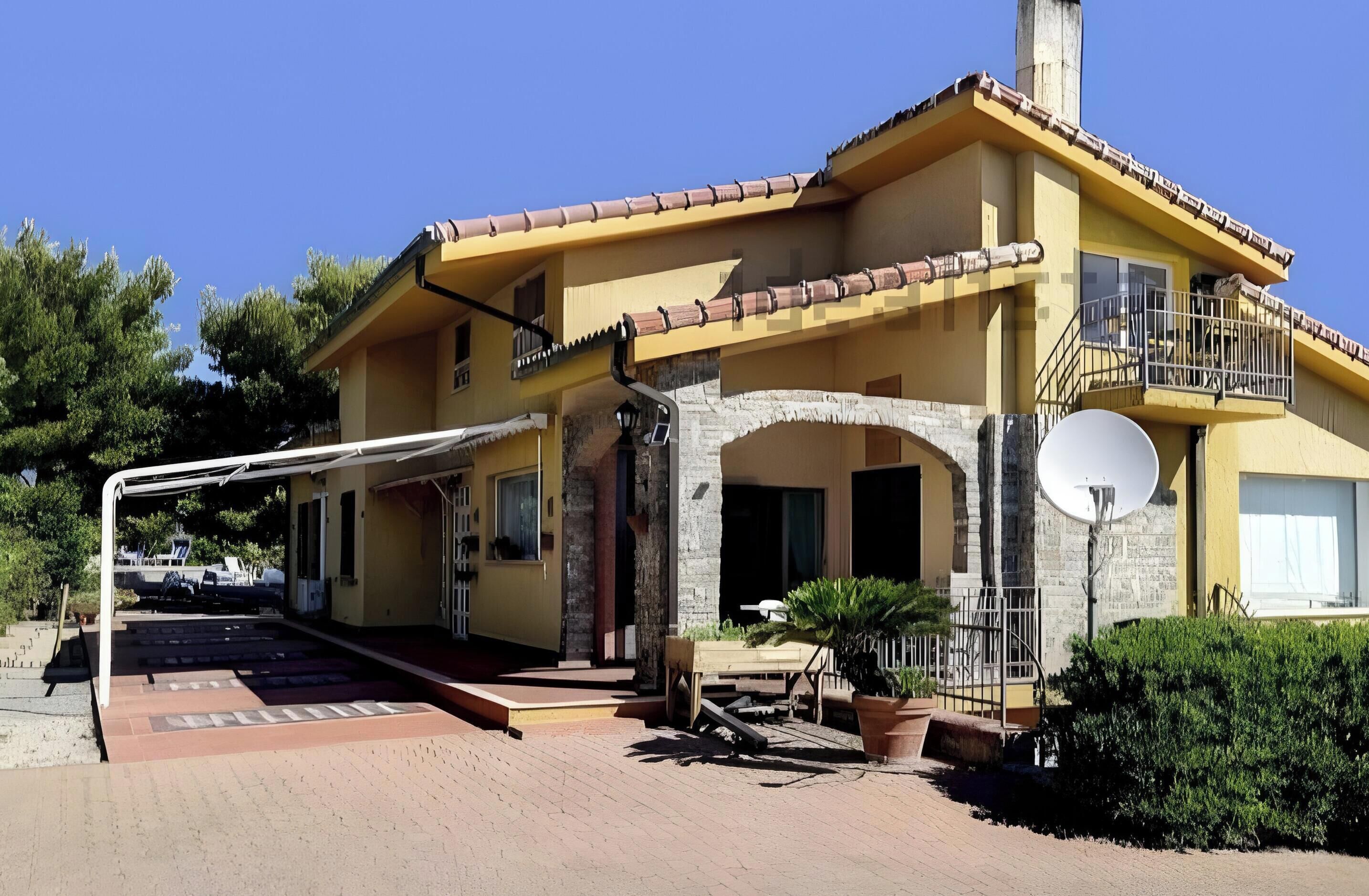 Um edifício de dois andares com fachada amarela, varanda no andar de cima e antena parabólica no lado direito.