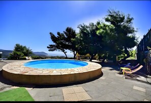 A circular pool with a stone edge, surrounded by a patio area with lounge chairs and a view of the mountains. - Apartment 'Aurora' with Sea View, Shared Pool and Wi-Fi (Poggi)