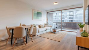 A modern living room with a dining area, a sofa, a glass coffee table, and a view of a cityscape through large windows. - Luxury Living w/ Rooftop Pool & Garage by HostWise (Vila Nova de Gaia)