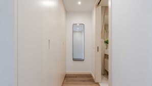 A narrow hallway with a wooden floor, white walls, and a mirror on the wall. - Luxury Living w/ Rooftop Pool & Garage by HostWise (Vila Nova de Gaia)