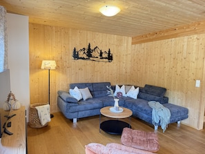 Una sala de estar acogedora con techo de madera, un sofá modular, una mesita redonda y un adorno en la pared.