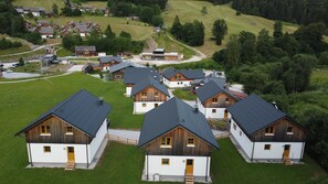 A cluster of wooden cabins with sloped roofs, surrounded by green fields and trees.