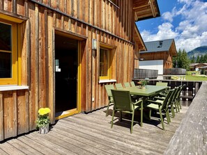 A wooden building with a deck, a table with chairs, and a door.