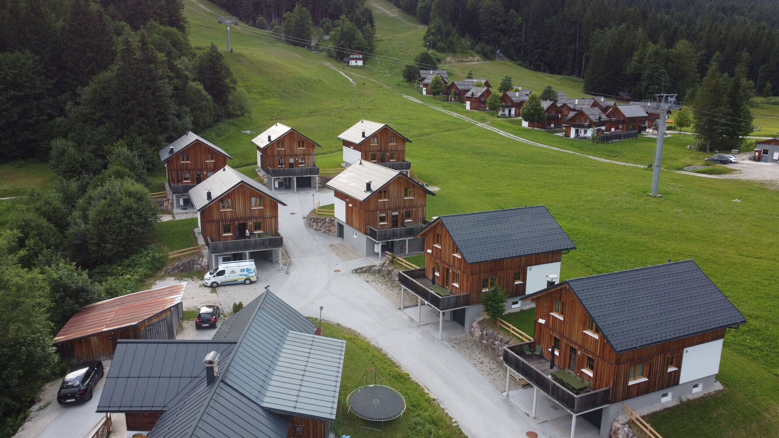 A cluster of wooden cabins with balconies, a paved driveway, and a grassy hill in the background.