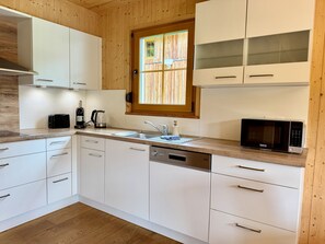 A modern kitchen with white cabinets, a built-in dishwasher, a microwave, and a window with blinds.