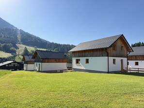 Un paisaje rural con un edificio blanco de fachada de madera, un edificio negro con techo metálico y un campo cubierto de hierba.