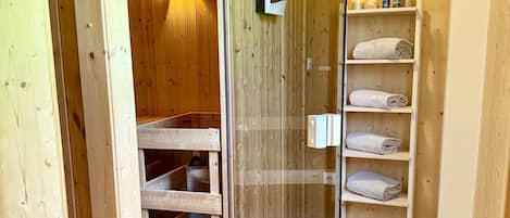 A wooden interior with a glass door leading to a room, shelves with towels, and a wooden floor.