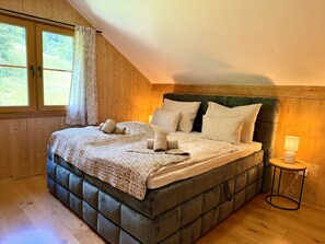 Un dormitorio con techo de madera, cama con cabecera tapizada en verde y ventana con cortinas.