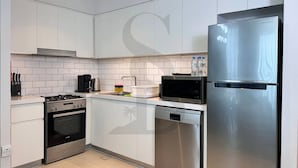 Une cuisine moderne avec des meubles blancs, des appareils en acier inoxydable, notamment un réfrigérateur, un four à micro-ondes et un lave-vaisselle, ainsi qu’une cuisinière à gaz.