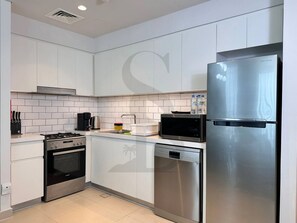 A modern kitchen with white cabinetry, stainless steel appliances including a refrigerator, microwave, and dishwasher, and a gas stove. - Amazing Water View Luxury 2 Br Prime Location (Dubai)