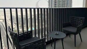 Un balcon avec deux chaises et une petite table, donnant sur un paysage urbain dominé par des immeubles de grande hauteur.
