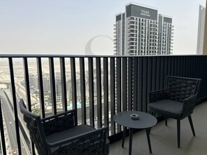 A balcony with two chairs and a small table, overlooking a cityscape with high-rise buildings. - Amazing Water View Luxury 2 Br Prime Location (Dubai)
